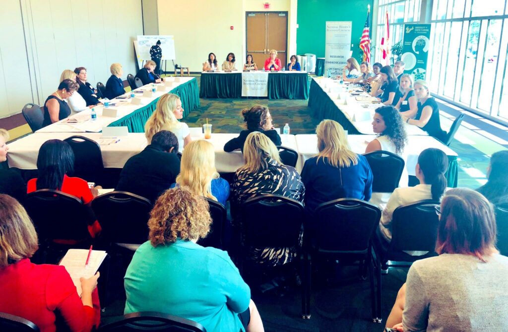 A group of women at a roundtable and with audience.